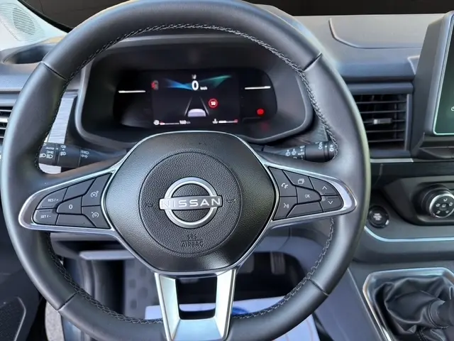 Vue rapprochée du volant noir en cuir synthétique d'un Nissan Primastar 2025 avec tableau de bord numérique en arrière-plan.