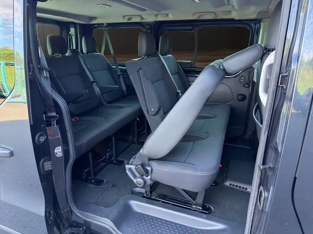 Vue intérieure côté droit du Nissan Primastar gris foncé, montrant les sièges arrière avec une banquette relevée.