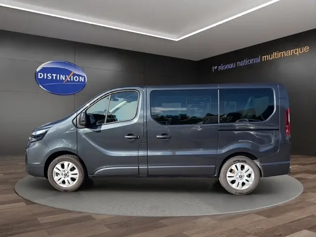 Vue latérale droite d'un Nissan Primastar gris foncé avec vitres teintées, présenté en intérieur showroom.