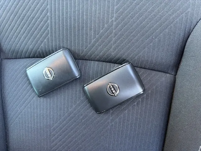 Gros plan sur deux clés Nissan noires posées sur un siège tissu gris foncé à motifs diagonaux.