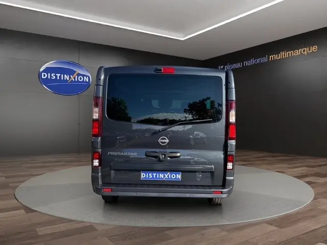 Vue arrière d’un Nissan Primastar gris foncé, avec portes arrière vitrées et logo Distinxion visible sur le pare-chocs.
