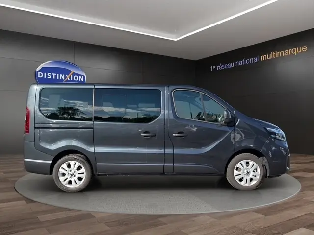 Profil latéral droit d’un Nissan Primastar gris foncé 2025 en intérieur, avec vitres teintées et jantes acier.