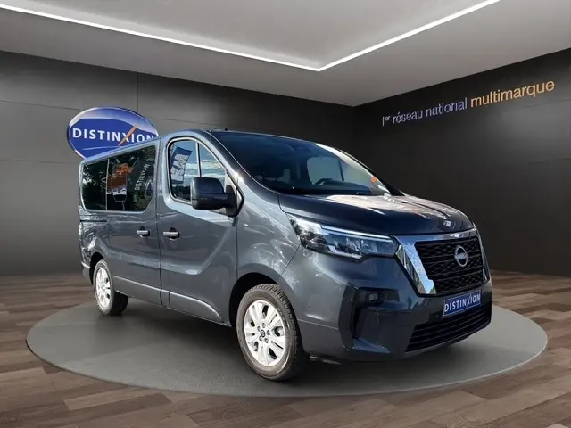 Vue 3/4 avant d'un Nissan Primastar gris foncé avec calandre noire et logo chrome, présenté en showroom.