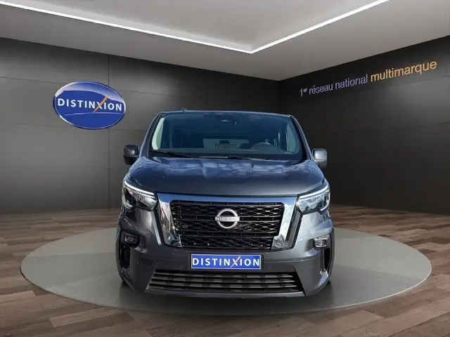 Vue frontale d'un Nissan Primastar gris foncé avec calandre noire et logo Nissan bien visible en showroom.