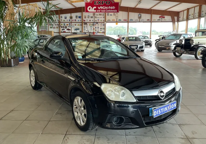 Opel Tigra Twintop noir vue 3/4 avant droit dans un showroom avec plusieurs voitures anciennes en arrière-plan