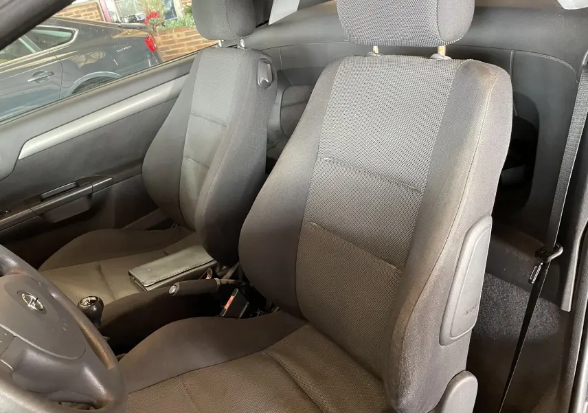 Vue intérieure des sièges avant en tissu gris foncé de l'Opel Tigra Twintop noir de 2006, côté conducteur visible.