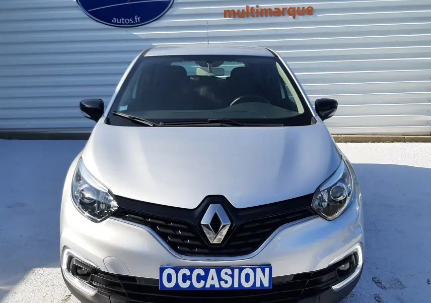 Vue frontale d'un Renault Captur gris platine métal 2019 avec plaque "OCCASION" devant un mur métallique.