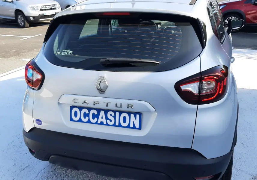 Vue 3/4 arrière droite d'un Renault Captur gris platine métallisé avec feux LED et plaques "OCCASION" sur parking.