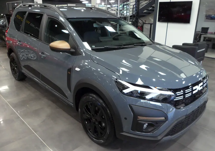 Vue 3/4 avant d'un Dacia Jogger TCe 110 gris urbain avec rétroviseurs bronze et jantes noires en showroom.