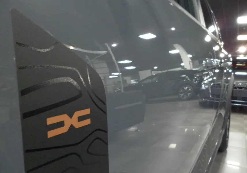 Détail du logo EXTREME orange sur la porte côté droit d'un Dacia Jogger gris urbain en intérieur showroom.
