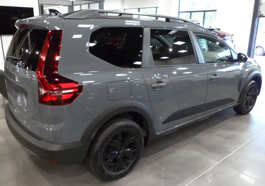 Vue 3/4 arrière droite d'un Dacia Jogger TCe 110 gris urbain avec jantes noires et vitres teintées en showroom.