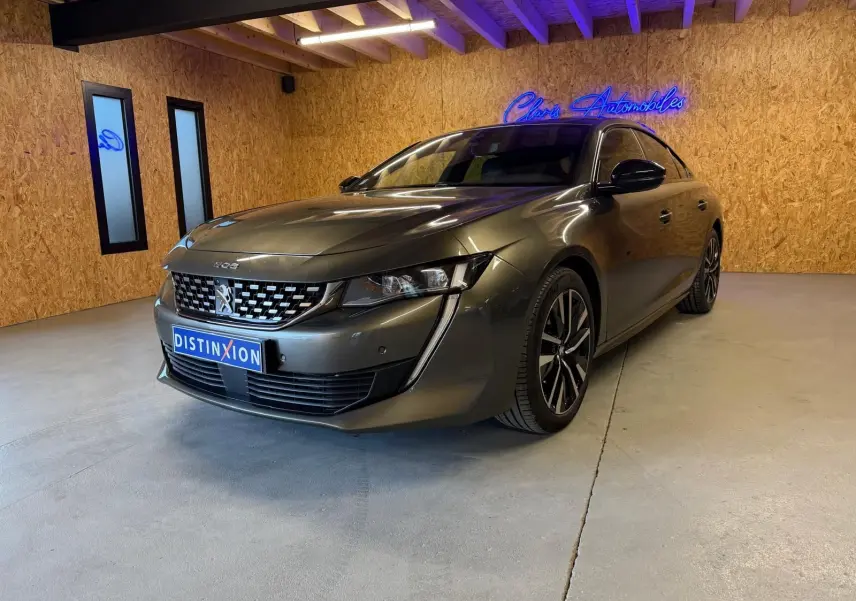 Peugeot 508 gris en 3/4 avant droit dans un intérieur avec murs en bois et éclairage néon bleu.
