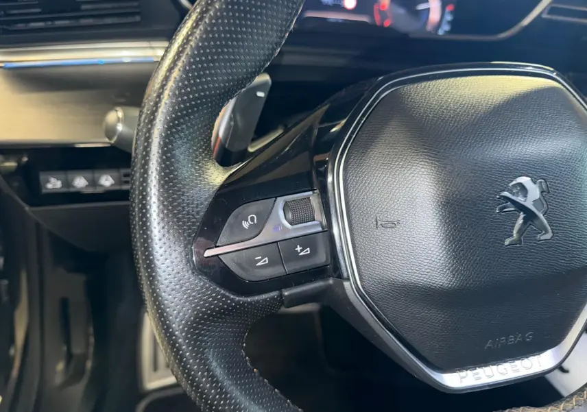 Gros plan sur le volant cuir perforé de la Peugeot 508 gris, avec commandes intégrées et logo lion au centre.