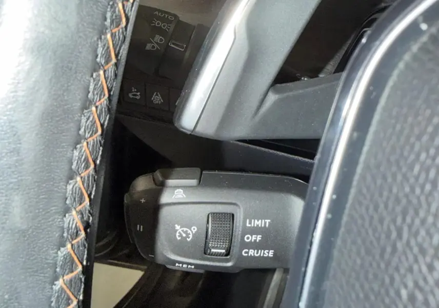 Gros plan sur la commande de régulateur de vitesse à gauche du volant cuir noir avec surpiqûres orange du Peugeot 508 gris.