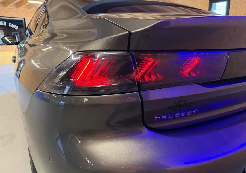 Vue 3/4 arrière gauche d'une Peugeot 508 gris métallisé avec feux arrière LED allumés en intérieur.