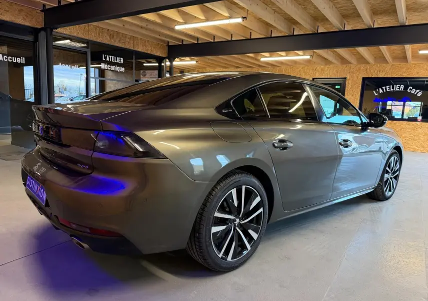 Vue 3/4 arrière droit d'une Peugeot 508 gris métallisé avec jantes alu et feux arrière LED, en intérieur showroom.