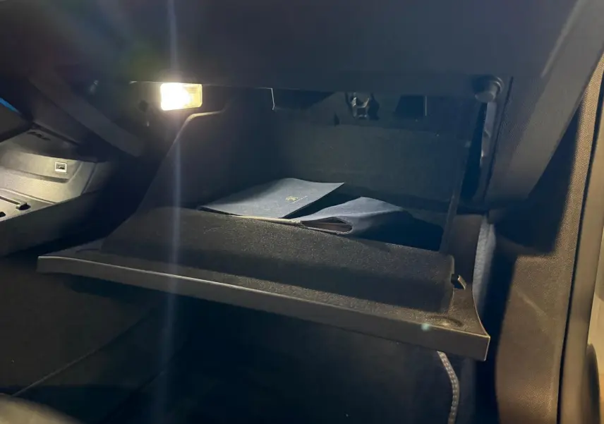 Gros plan sur la boîte à gants ouverte éclairée à l'intérieur de la Peugeot 508 gris, montrant des documents rangés.