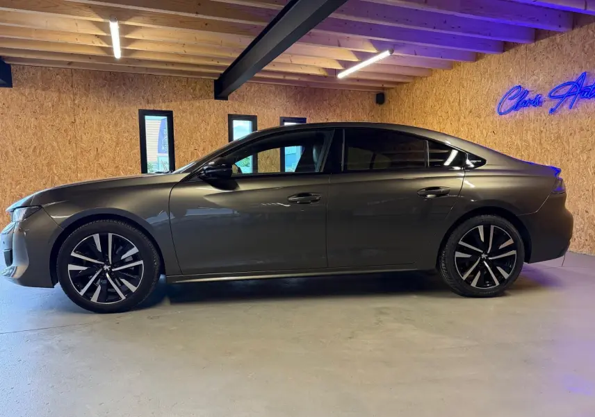 Peugeot 508 gris en profil droit dans un intérieur, avec jantes alliage noires et vitres teintées.