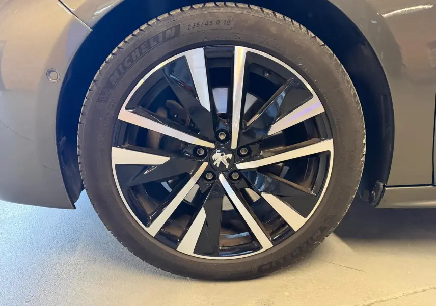 Gros plan sur la jante alu noire et argentée avec logo Peugeot centrale, sur roue avant droite d'une 508 gris 2019.