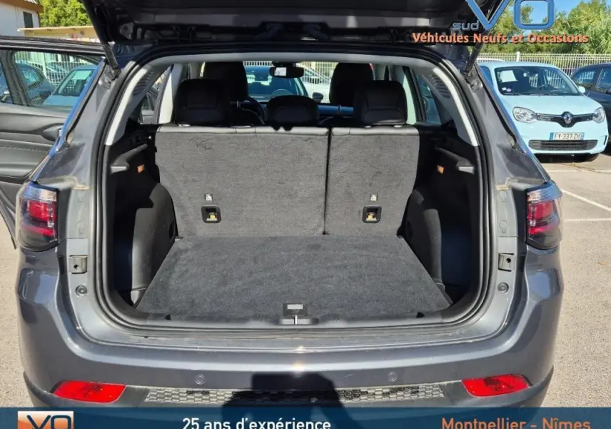 Coffre ouvert d’un Jeep Compass gris 3/4 arrière, montrant l’espace de chargement et les sièges arrière rabattus.