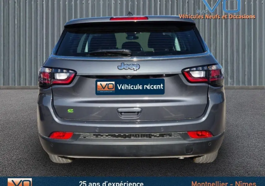 Vue arrière d'un Jeep Compass gris 2024 avec feux LED et logo e-Hybrid visible sur un fond neutre.