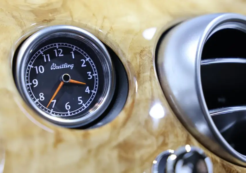 Gros plan sur l'horloge Breitling intégrée au tableau de bord en bois clair d'une Bentley Continental Flying Spur.