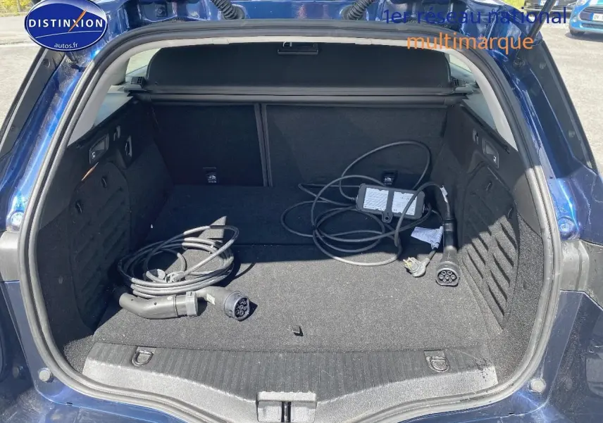 Coffre ouvert en vue arrière d’une Renault Mégane IV Estate bleu avec câbles de recharge hybride visibles.