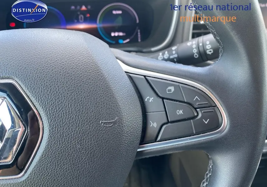 Gros plan sur le volant multifonction noir de la Renault Mégane IV Estate, avec commandes intégrées et tableau de bord numérique en arrière-plan.