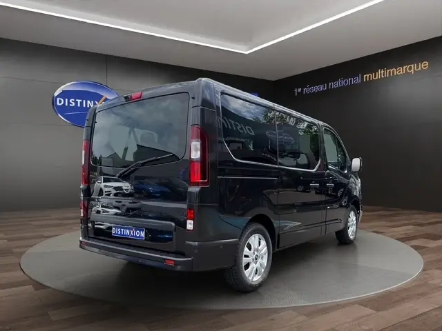 Vue 3/4 arrière droite d'un Nissan Primastar noir 2025 en showroom avec vitres teintées et jantes argentées.