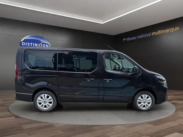Vue de profil droit du Nissan Primastar noir 2025 avec portes latérales vitrées dans un showroom.