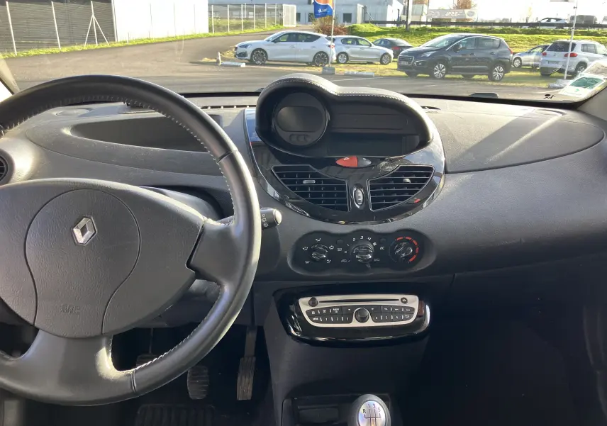 Vue intérieure du tableau de bord noir de la Renault Twingo II 75CH ESS 2011 avec volant et commandes centrales visibles.