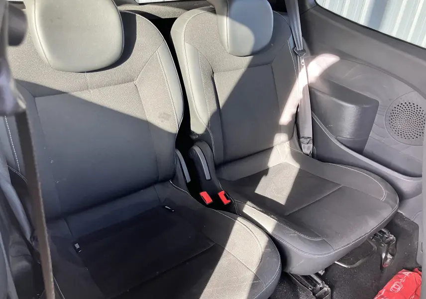 Vue intérieure sur les sièges arrière noirs de la Renault Twingo II 75CH ESS de 2011 avec ceintures et porte latéral visible.