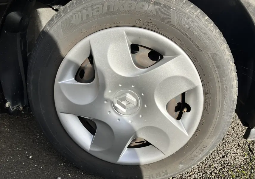 Gros plan sur la roue avant droite d'une Renault Twingo II noire de 2011 avec enjoliveur argenté et logo Renault central.