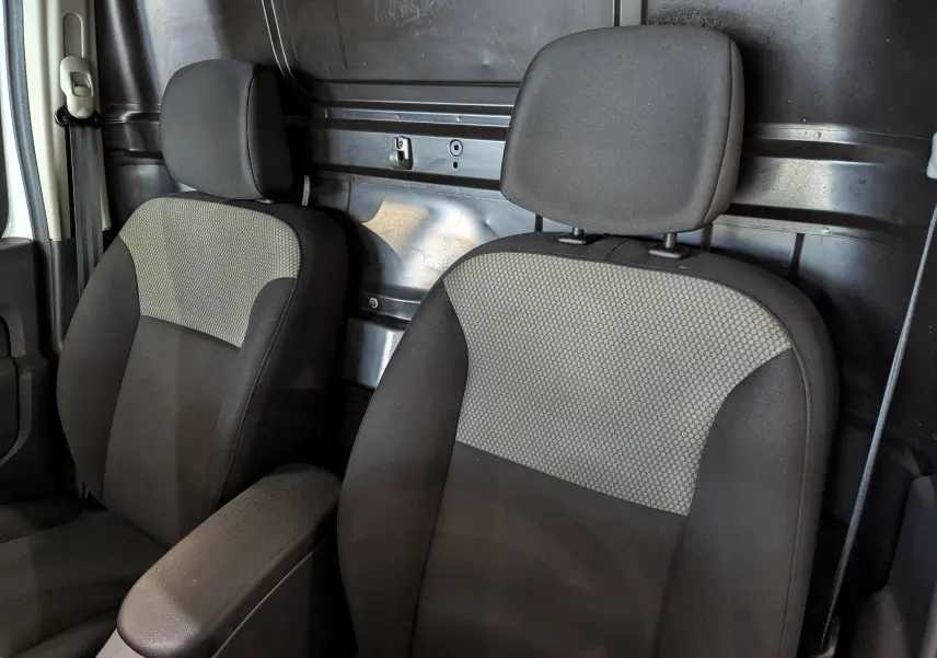 Gros plan sur les sièges avant en tissu gris et noir du Renault Kangoo Express blanc, avec cloison métallique arrière visible.