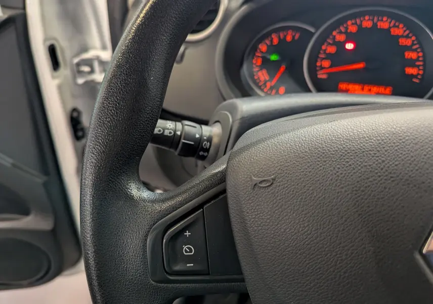 Gros plan sur le volant noir et le tableau de bord éclairé du Renault Kangoo Express blanc, côté conducteur ouvert.