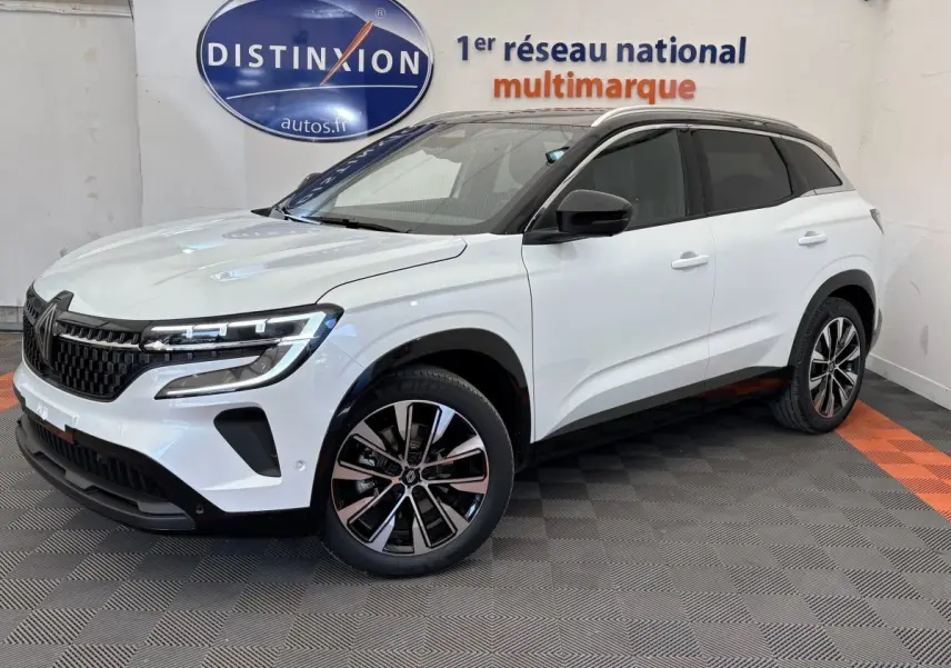 Vue 3/4 avant droite du Renault Austral blanc avec jantes alliage et toit noir dans un showroom multimarque.