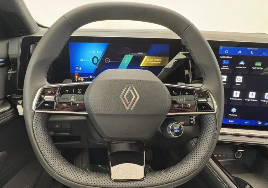 Vue frontale du volant cuir perforé et des écrans numériques du tableau de bord du Renault Austral blanc hybride 2025.