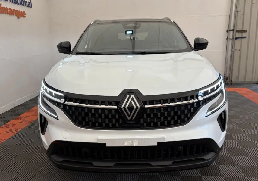 Vue frontale d'un Renault Austral blanc avec calandre noire et feux LED allumés dans un showroom.