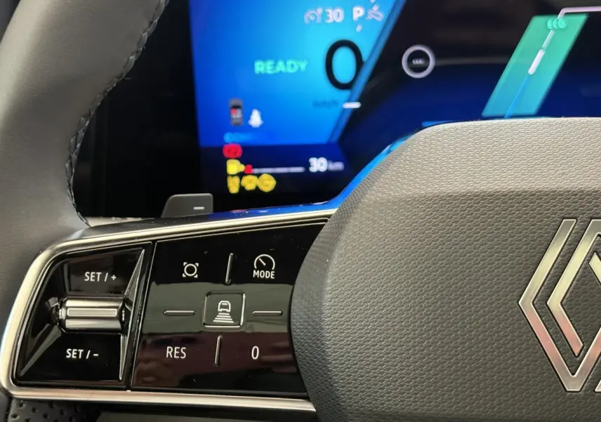 Gros plan sur le volant gris du Renault Austral 2025 avec commandes multifonctions et tableau de bord numérique bleu en arrière-plan.