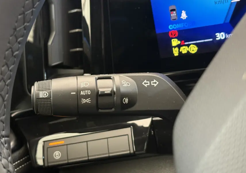 Gros plan sur la commande des feux et clignotants à gauche du volant dans le tableau de bord noir du Renault Austral blanc.