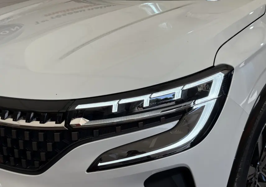 Gros plan sur le phare avant droit allumé du Renault Austral blanc, soulignant la calandre noire et les lignes modernes du capot.
