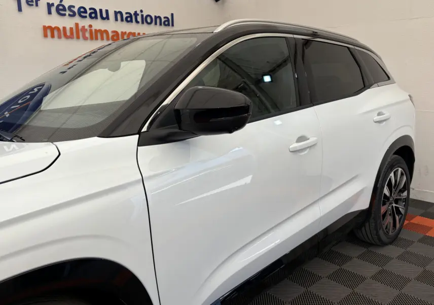 Profil côté gauche du Renault Austral blanc avec toit noir et rétroviseur noir dans un showroom.