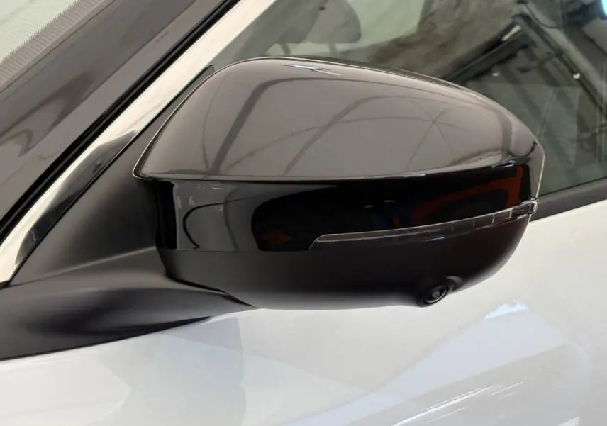 Rétroviseur côté gauche noir brillant avec caméra intégrée sur Renault Austral blanc, vue rapprochée du côté conducteur.