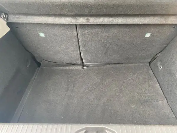 Coffre vide vu de face d'une Renault Clio V gris platine, montrant la moquette intérieure et les dossiers arrière rabattables.