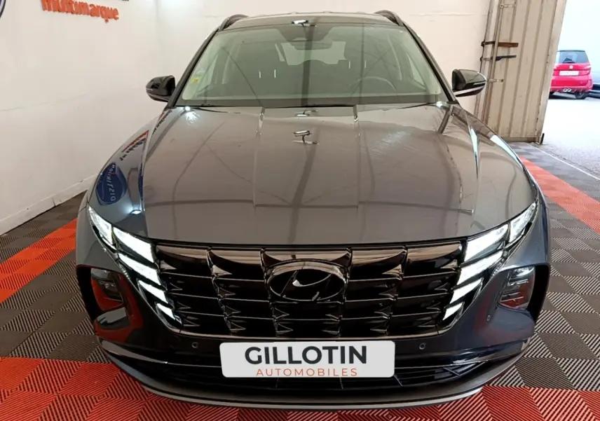 Vue avant d'un Hyundai Tucson gris foncé 2022 avec calandre noire et phares LED allumés dans un garage.