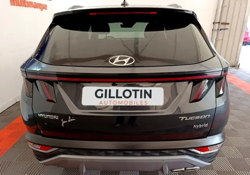 Vue arrière d’un Hyundai Tucson gris foncé hybride 2022 avec feux arrière en bandeau et logo Hyundai visible.