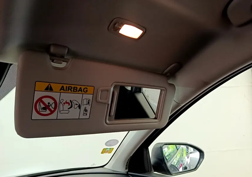 Détail intérieur montrant le pare-soleil côté conducteur avec miroir et avertissement airbag, rétro extérieur visible.