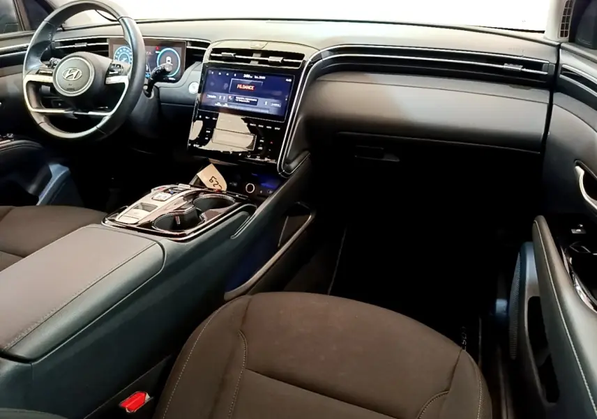Intérieur du Hyundai Tucson 1.6 Hybrid 230, vue côté passager, tableau de bord noir avec écran tactile central lumineux.