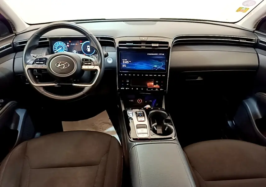 Vue intérieure avant du Hyundai Tucson 1.6 Hybrid 230 Creative 2022, tableau de bord noir avec écran tactile central et volant multifonctions.