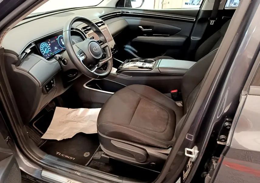 Vue intérieure côté conducteur du Hyundai Tucson gris foncé 2022, mettant en valeur le tableau de bord digital et les sièges noirs.
